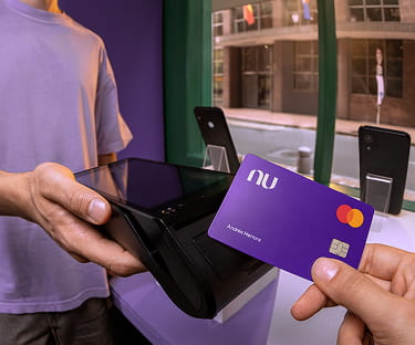 Dos mujeres sonriendo y sosteniendo una tarjeta de crédito Nu y un teléfono con la aplicación de Nu abierta